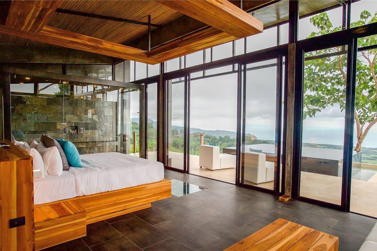 Un dormitorio moderno con una cama grande, una pared de piedra y vistas al exterior.