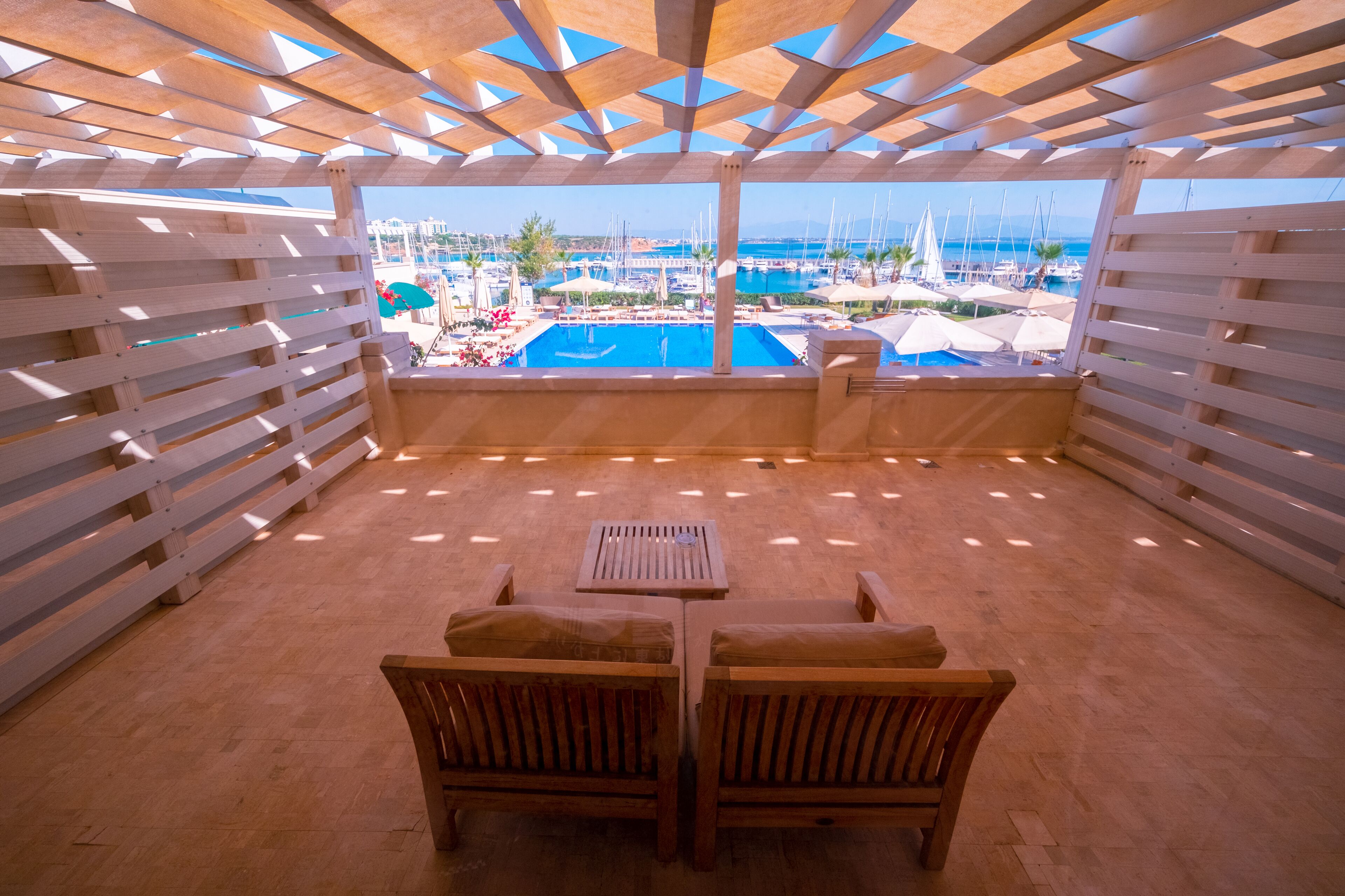 A wooden deck with a pool view, wooden furniture, and a clear sky.
