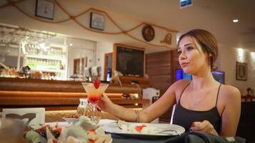 A woman sitting at a table with a drink and food in a restaurant.