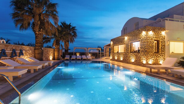 Una piscina con sillas de descanso y un edificio de piedra con luces.