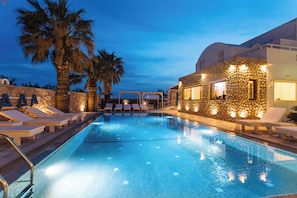 Una piscina con sillas de descanso y un edificio de piedra con luces.