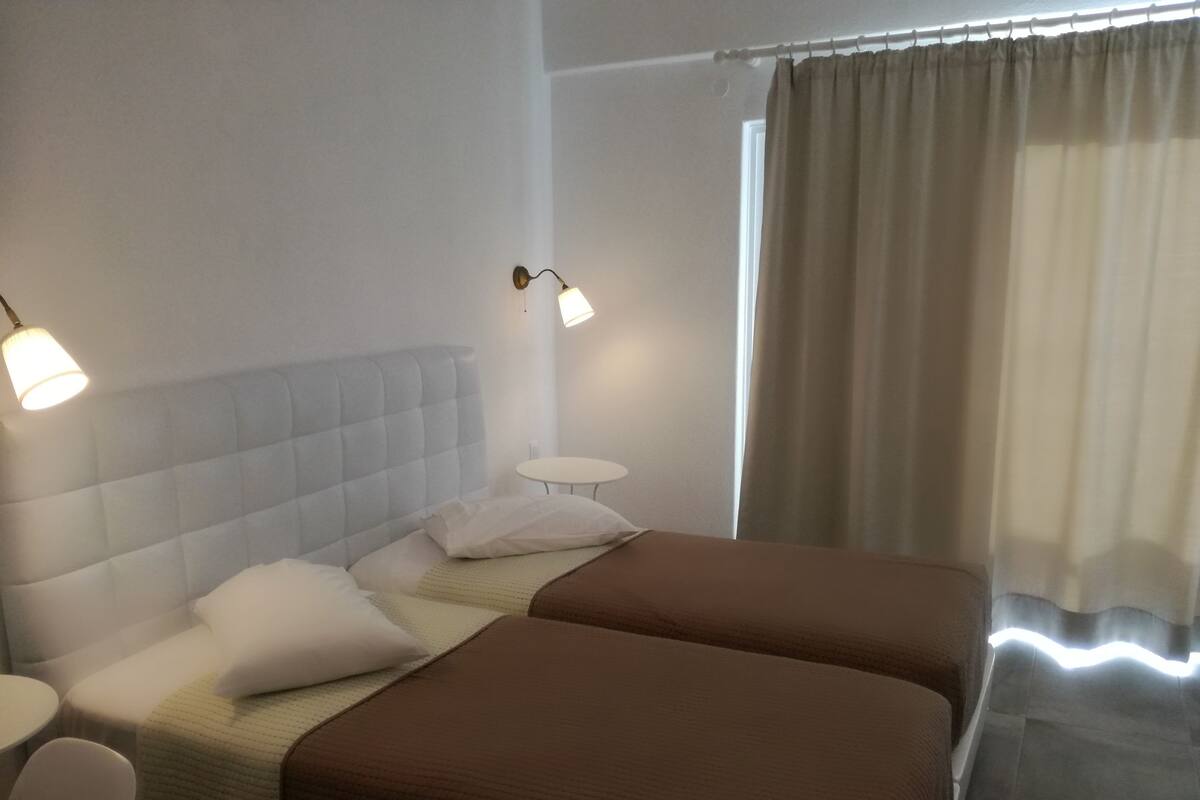 A hotel room with two beds, a small round table, and two wall-mounted lamps.