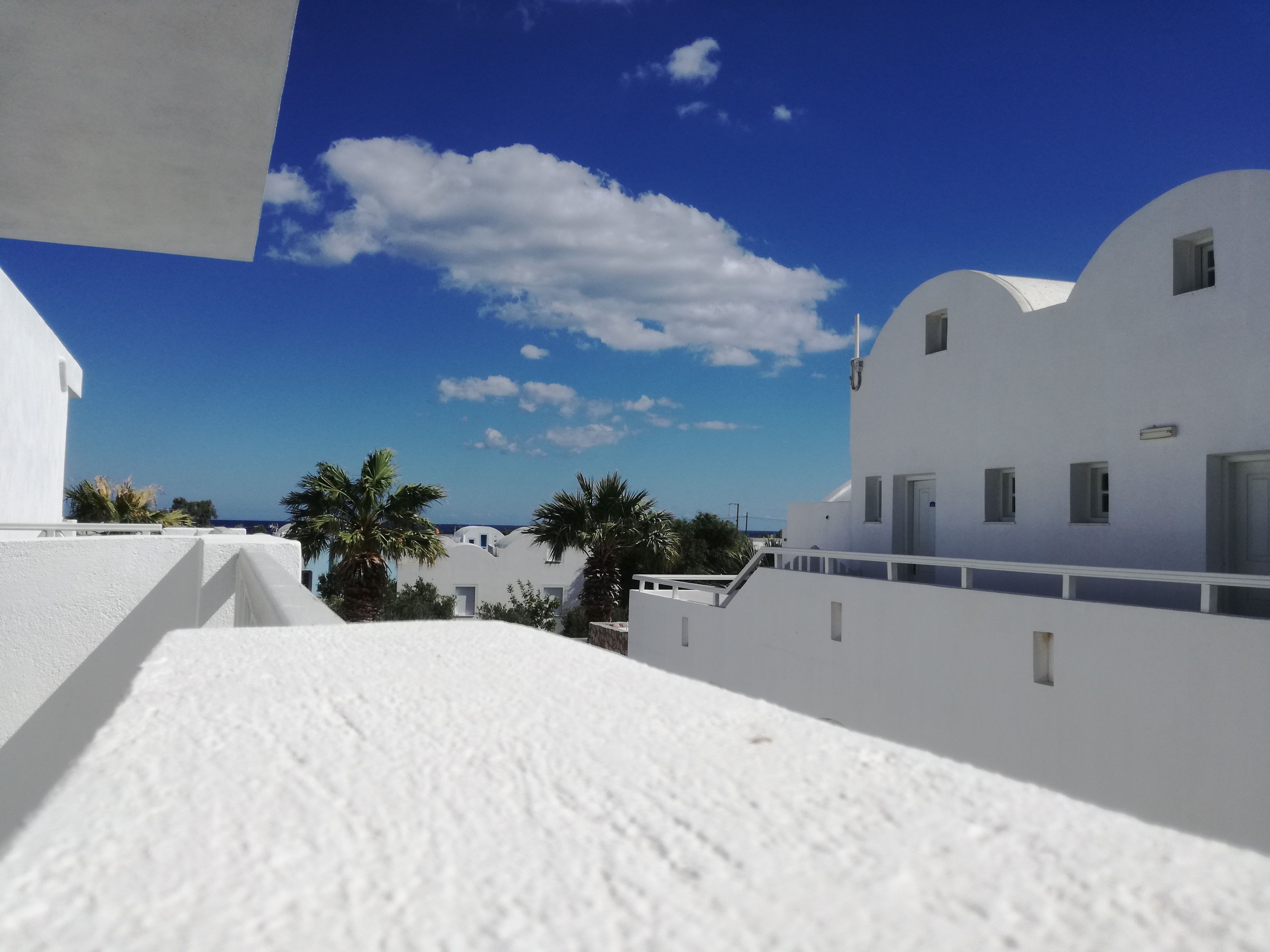 Un edificio blanco con techo plano, un balcón y un cielo azul despejado con nubes.