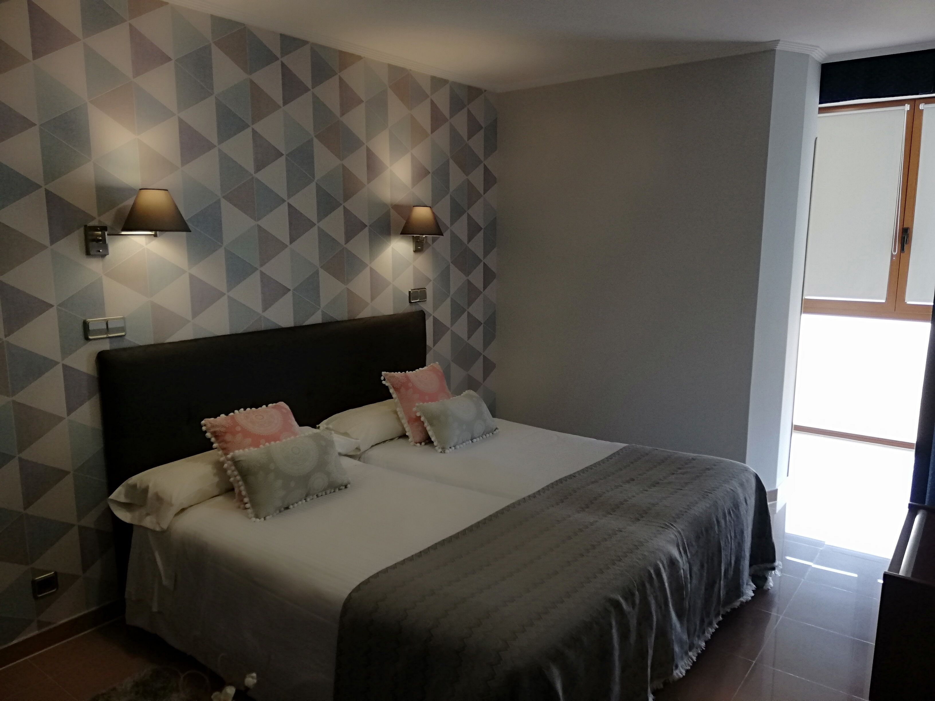 A bedroom with a bed, two wall-mounted lamps, and a geometric-patterned wall.