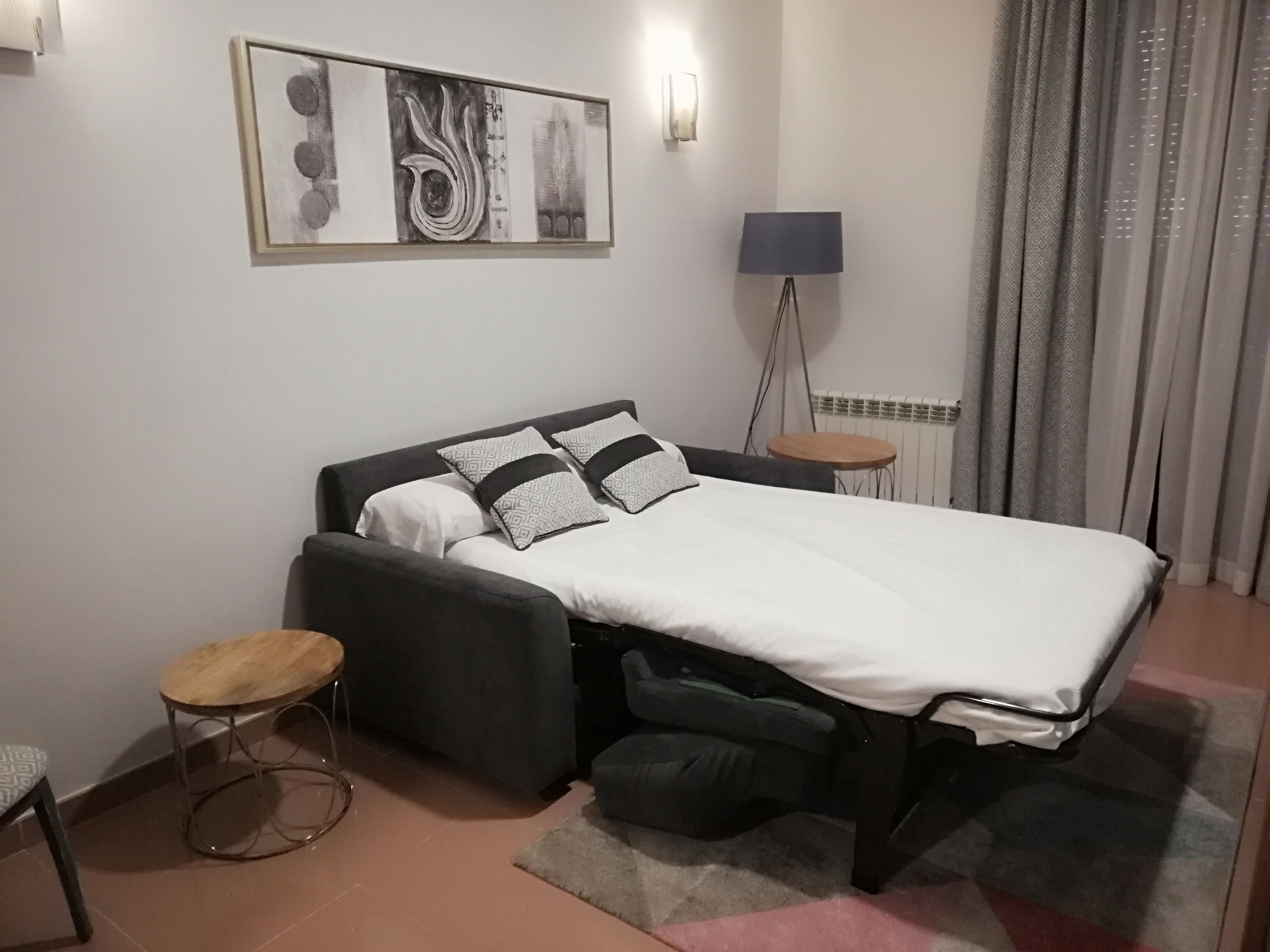 Un dormitorio moderno con una cama, una mesita de noche, una lámpara de pie y una obra de arte en la pared.