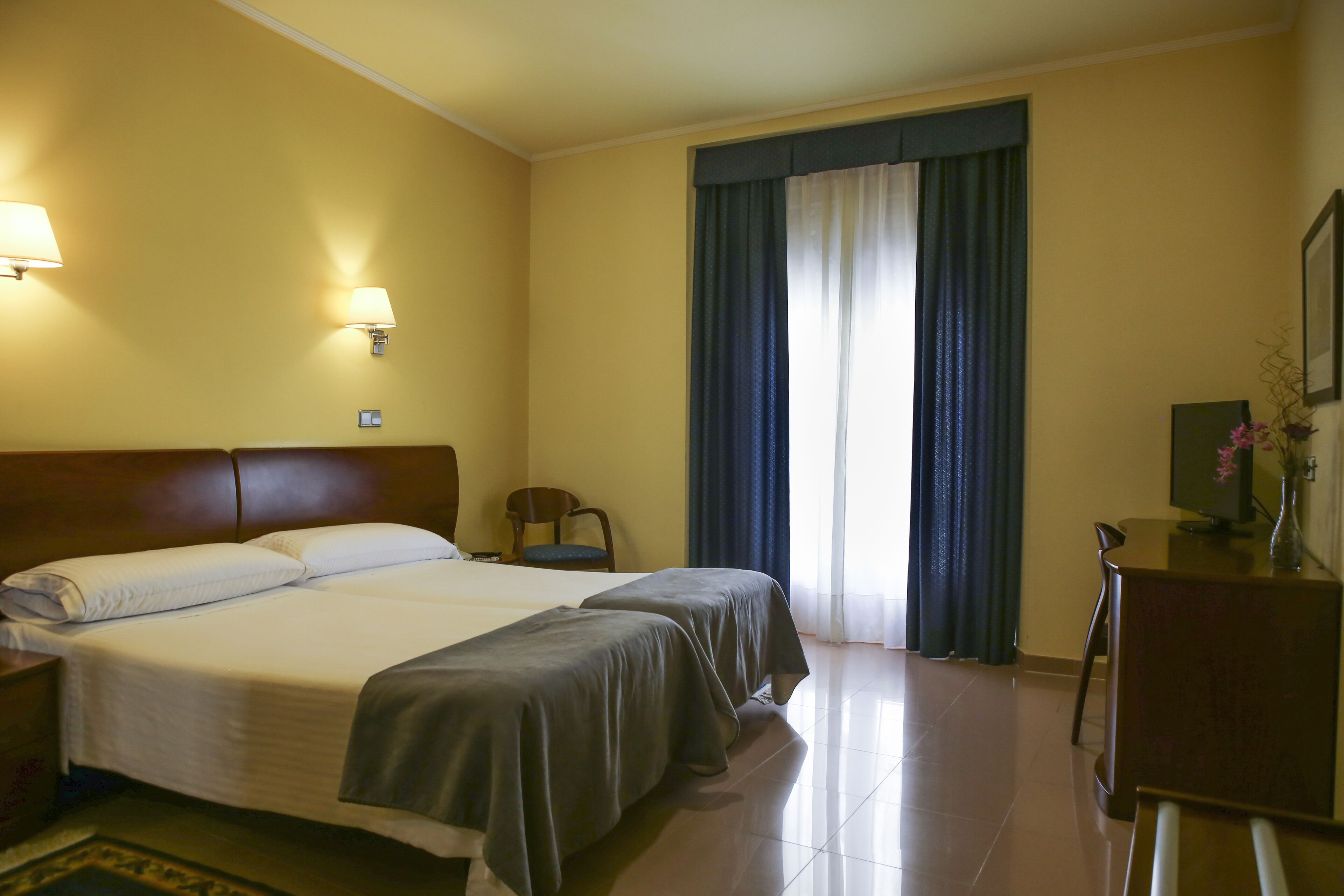 Een hotelkamer met twee bedden, een bureau, een stoel en een raam met gordijnen.
