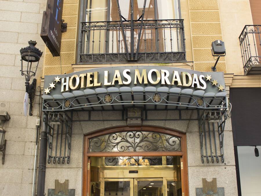 The entrance of Hotel Las Moradas with a classic facade, a glass door entrance, and a sign indicating handicap accessibility.