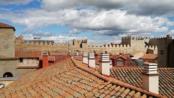 Terraço com telhas de terracota, uma parede de pedra e céu azul claro com nuvens.