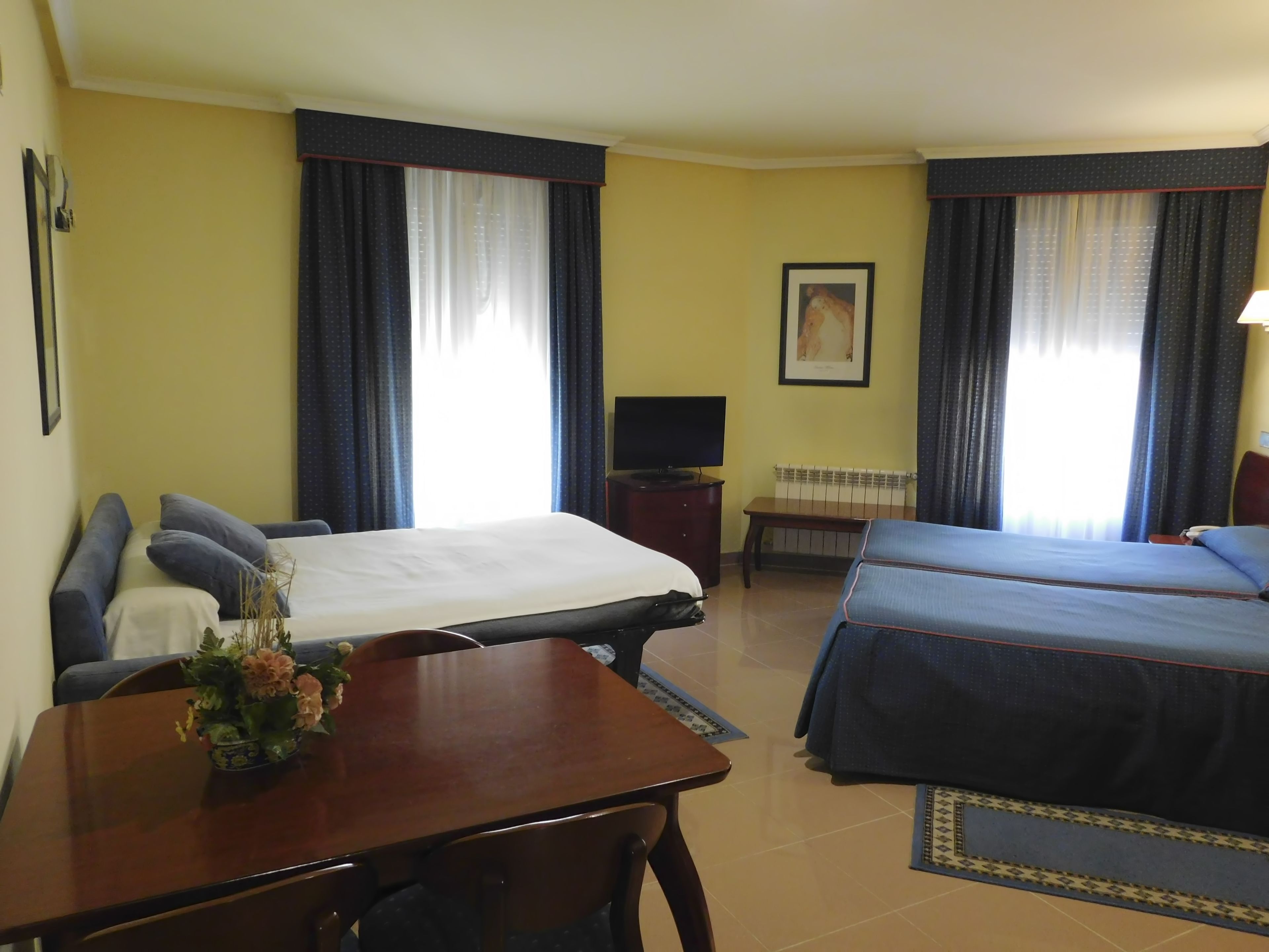 A hotel room with two beds, a desk, a chair, a TV, and a framed picture on the wall.