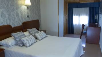 Una cama bien hecha con almohadones estampados, una lámpara de noche y un cabecero de madera.