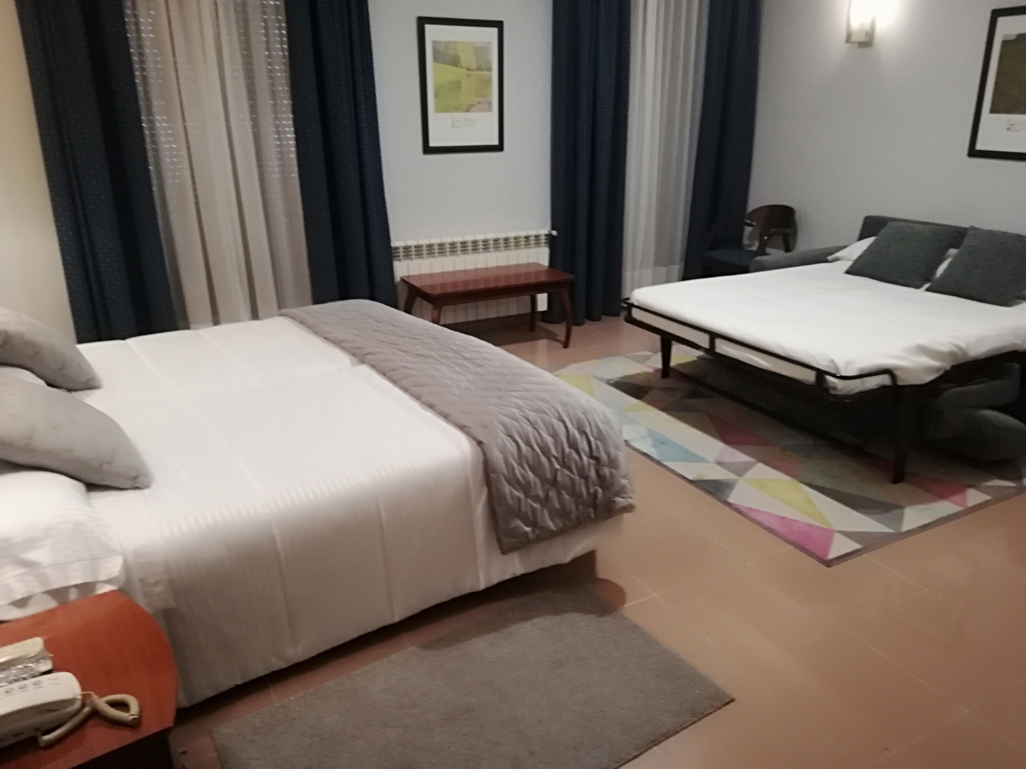 A hotel room with a double bed, a single bed, a desk with a telephone, a small table, and a chair.