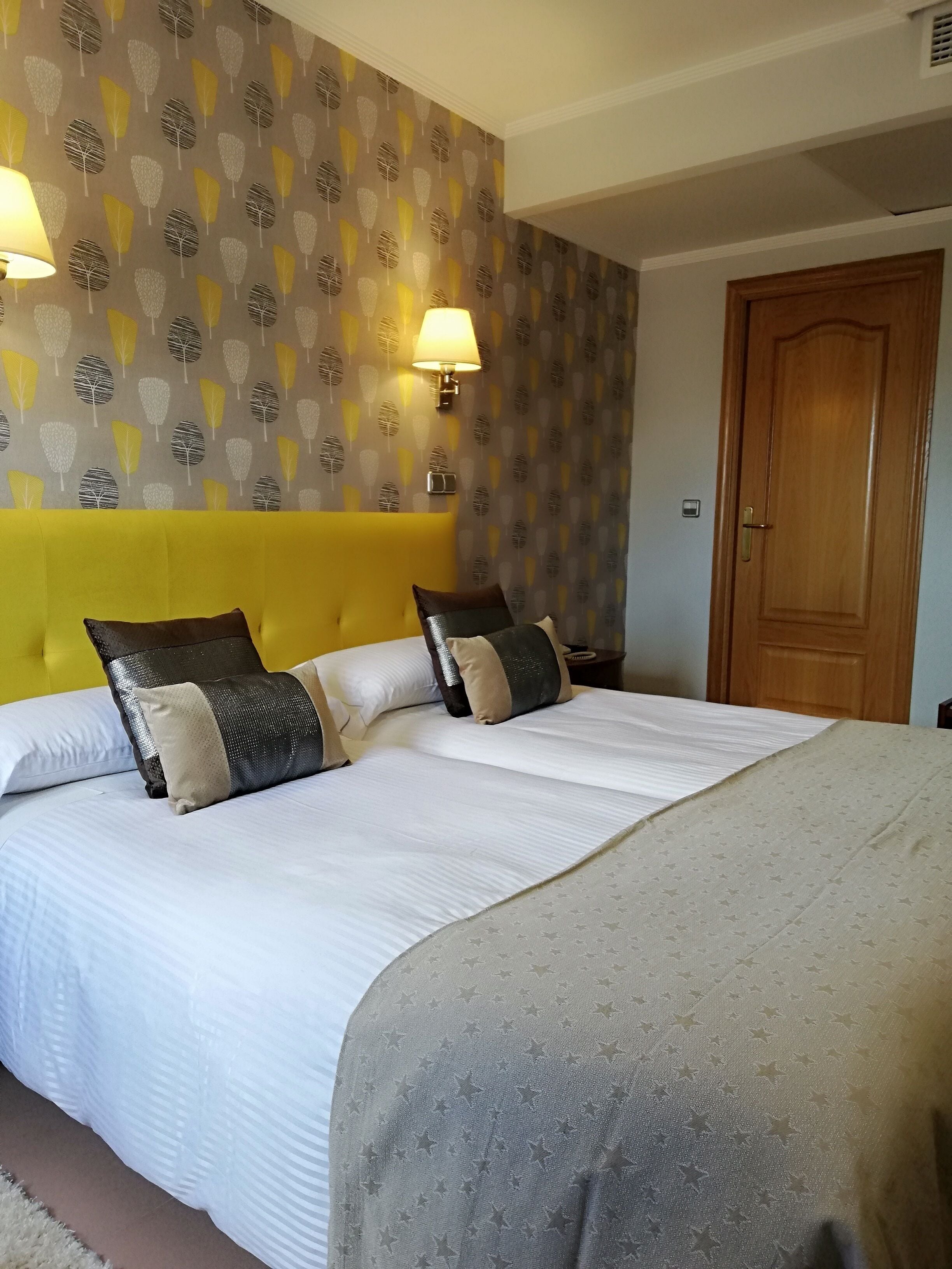 Ein Hotelzimmer mit einem Bett, zwei Nachttischlampen, einer Holztür und einem Wandpapier mit Muster.