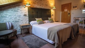 Quarto de hotel com uma cama grande, duas mesas de cabeceira, uma mesinha e uma cadeira.
