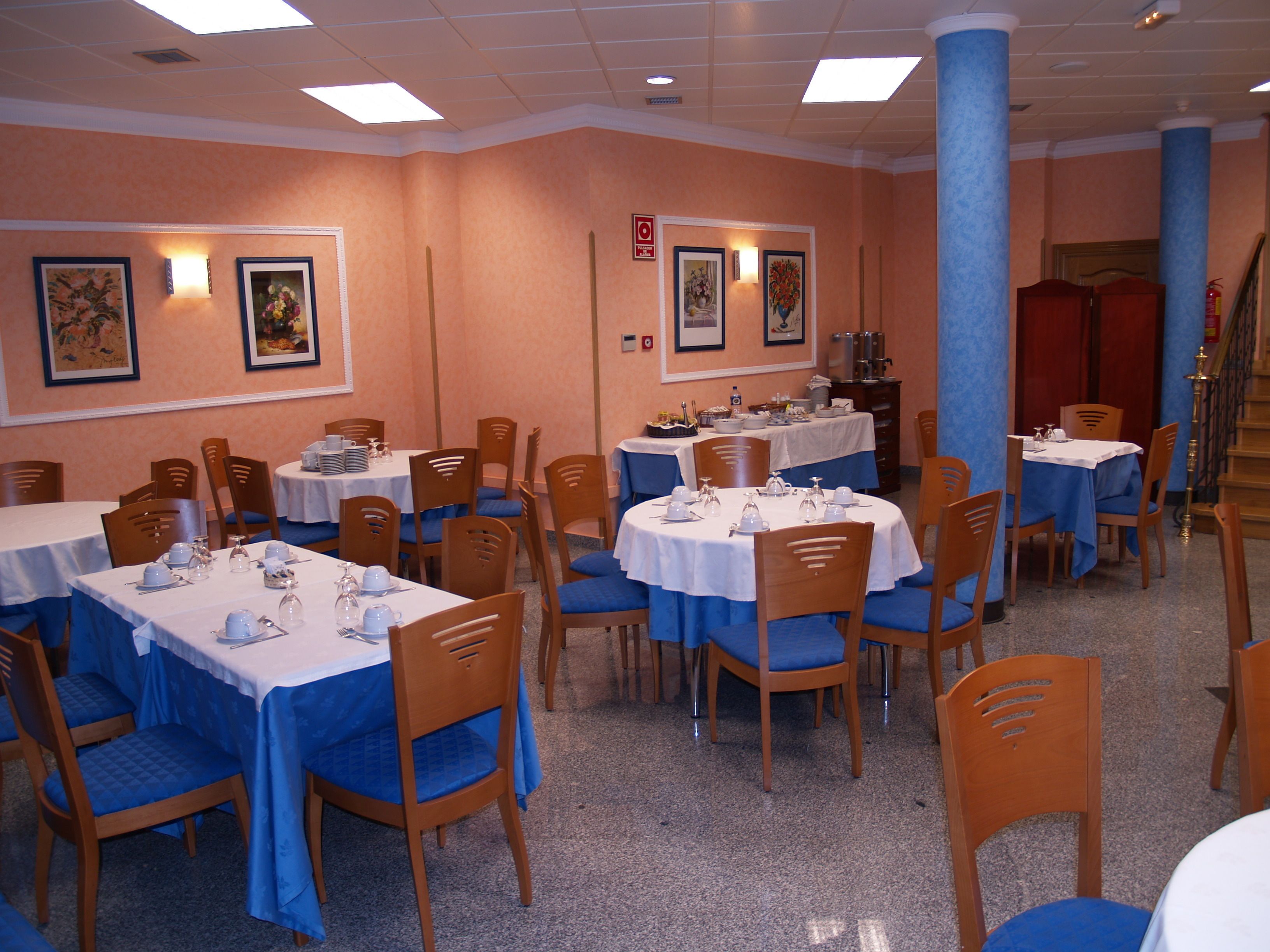 A dining area with multiple tables and chairs, each set with white tablecloths and blue chair covers.