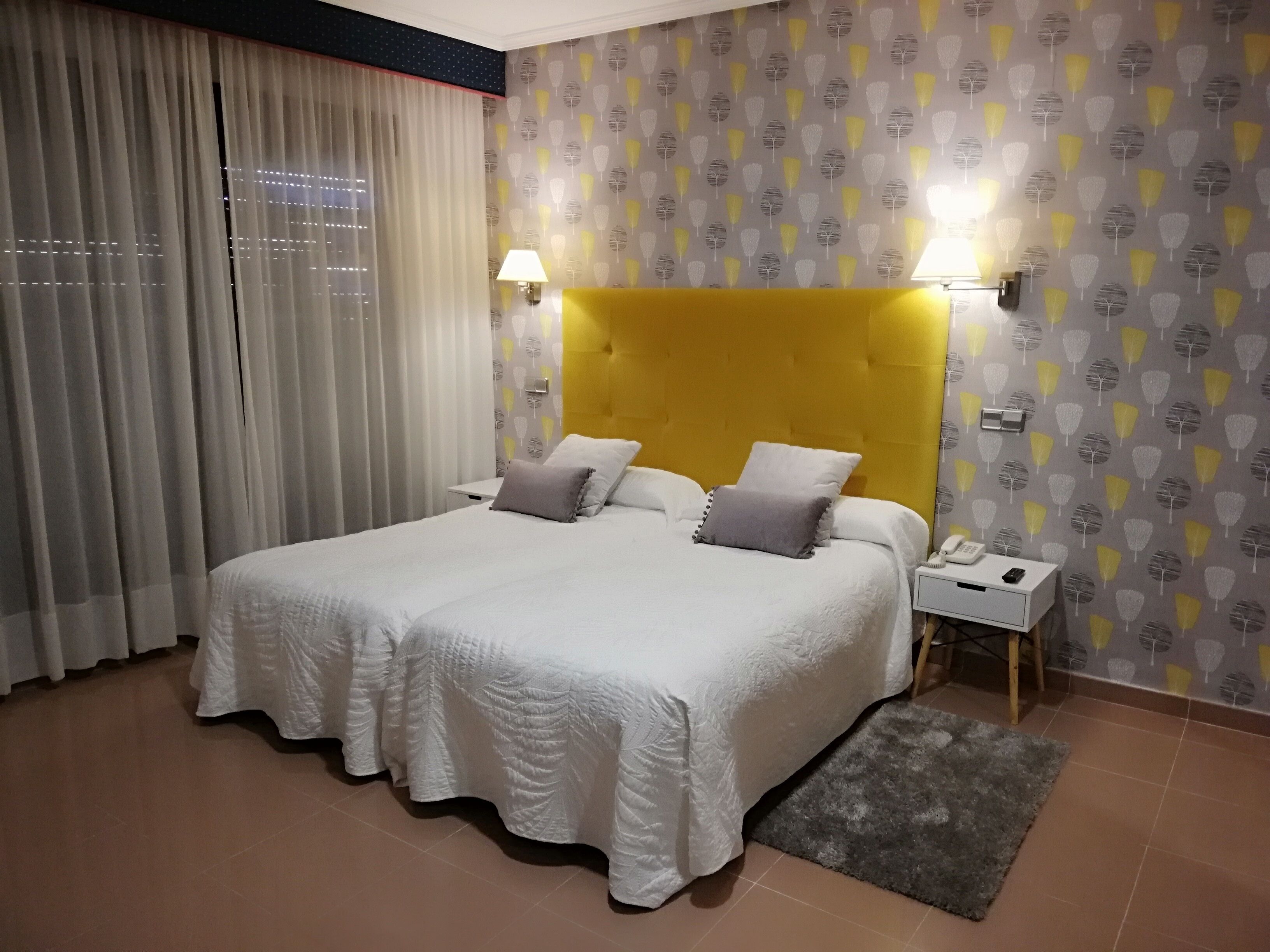 Ein Hotelzimmer mit einem großen Bett, einem Nachttisch, einer Lampe und einer Wand mit Muster.