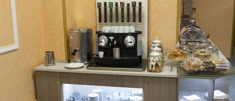 A coffee station with a Nespresso machine, various coffee cups, and a display of pastries and desserts.