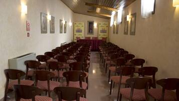 Un salón de conferencias con filas de sillas y mesas de madera, un atril y cuadros en las paredes.