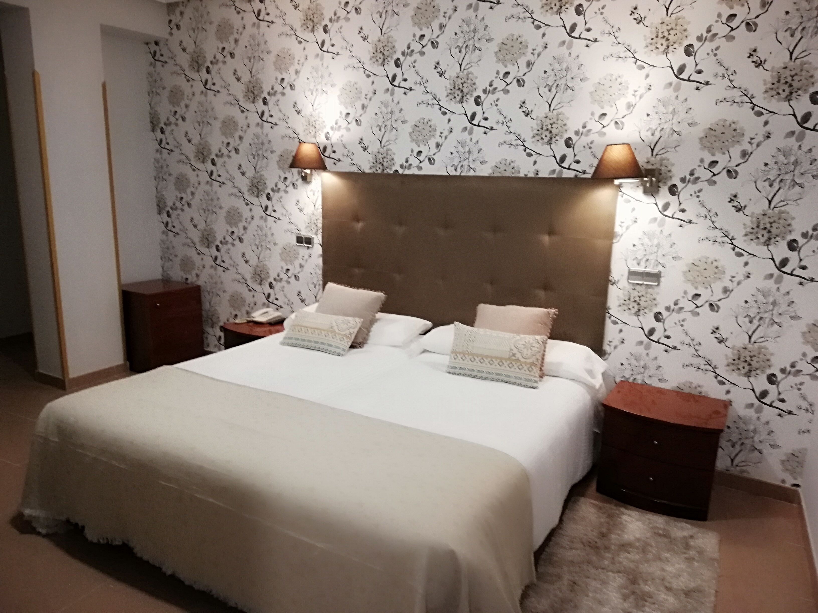 A bedroom with a large bed, two bedside tables, and a wall with floral wallpaper.
