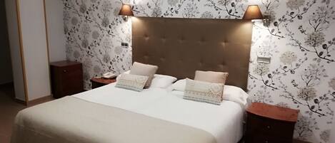 A bedroom with a large bed, two bedside tables, and a wall with floral wallpaper.