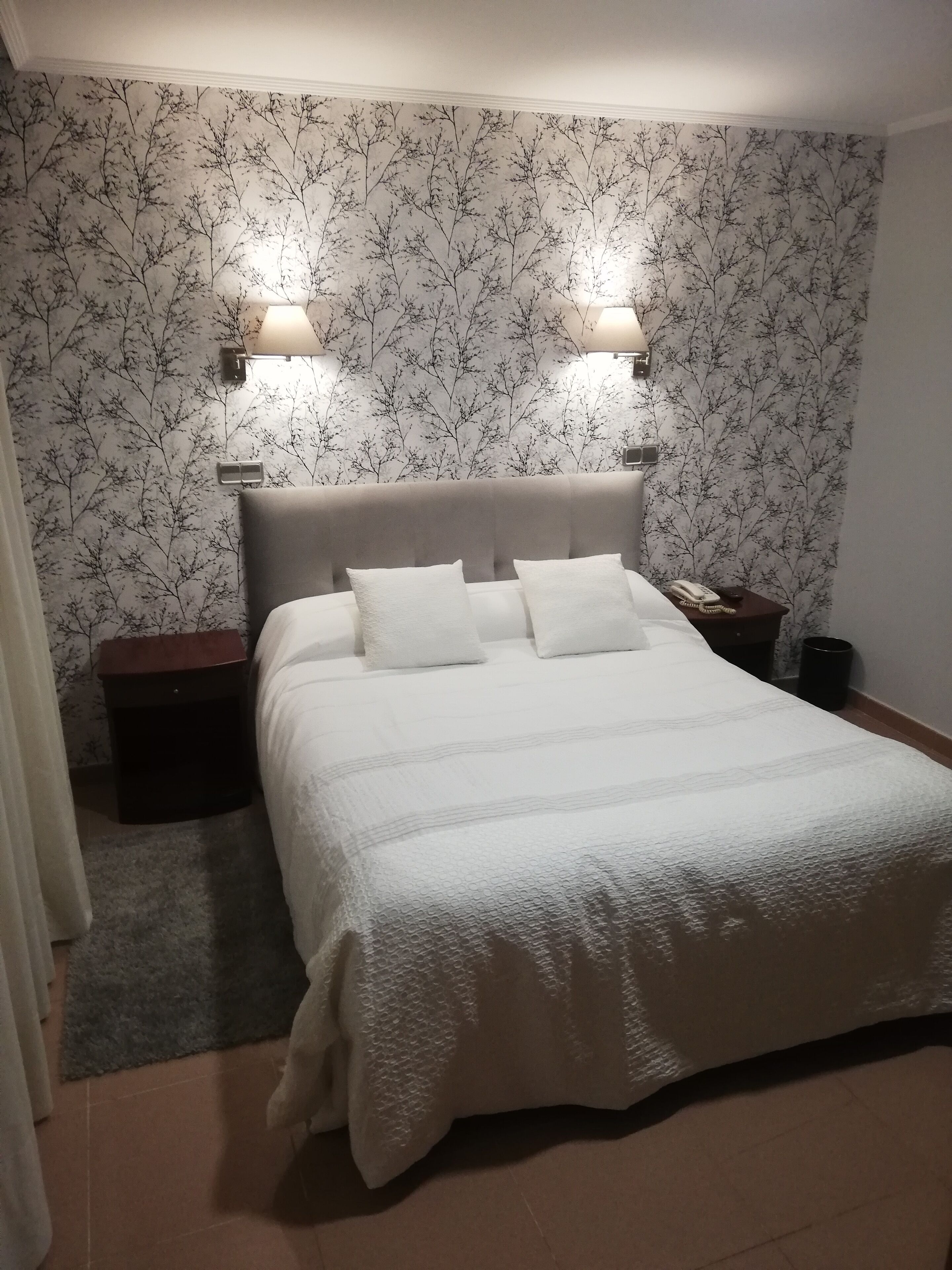 Un dormitorio con una cama, dos lámparas de noche, una mesita de noche y un cesto de basura.