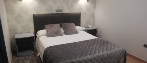 A bedroom with a bed, two bedside tables, a nightstand, a rug, and two wall-mounted lamps.