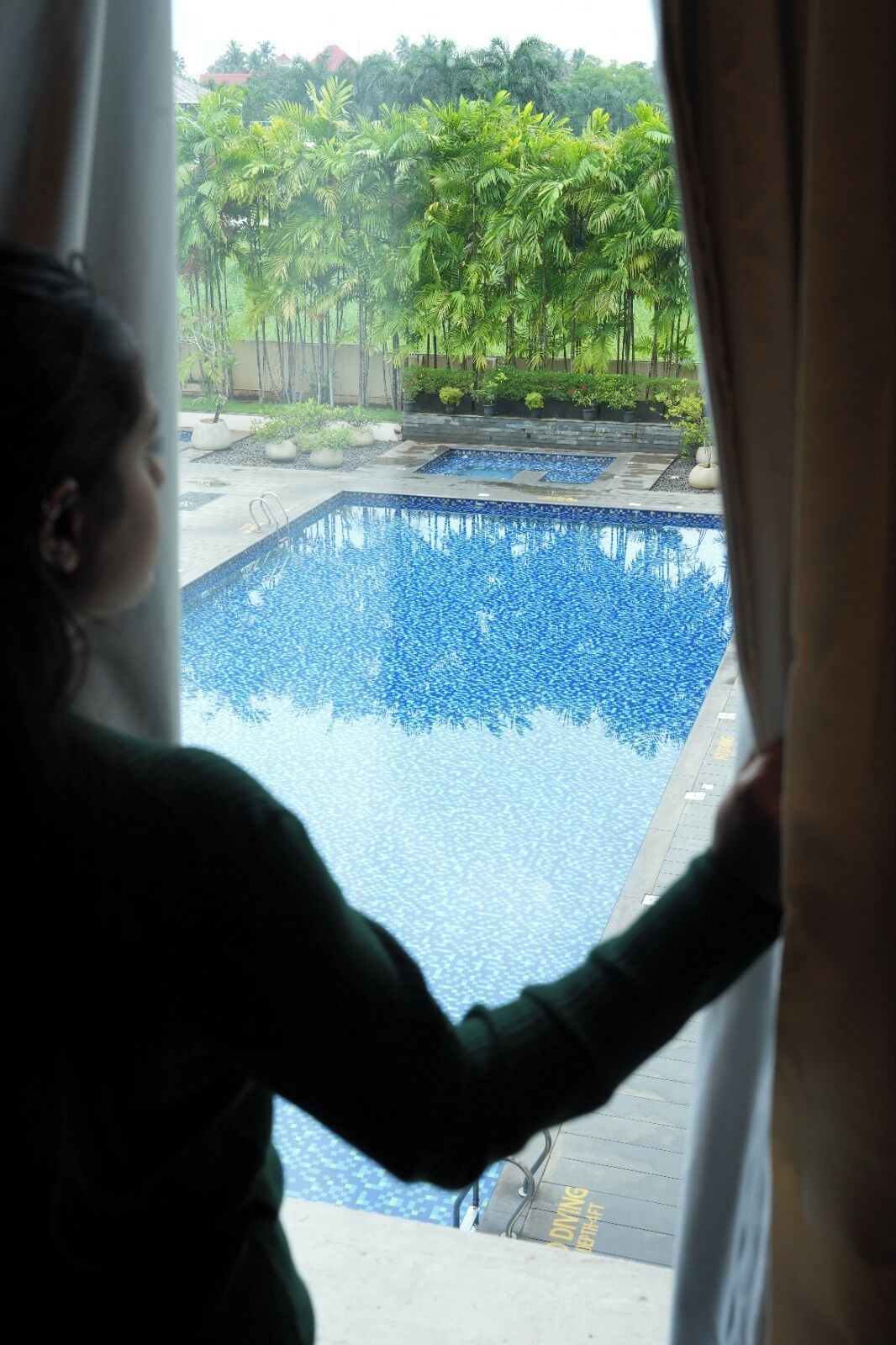 A view of a swimming pool with a tiled deck and palm trees in the background.