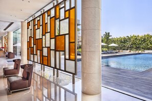 Un moderno vestíbulo de hotel con zona de piscina, destacando un amplio panel de vidrio con patrones geométricos, asientos cómodos y vistas a la piscina.