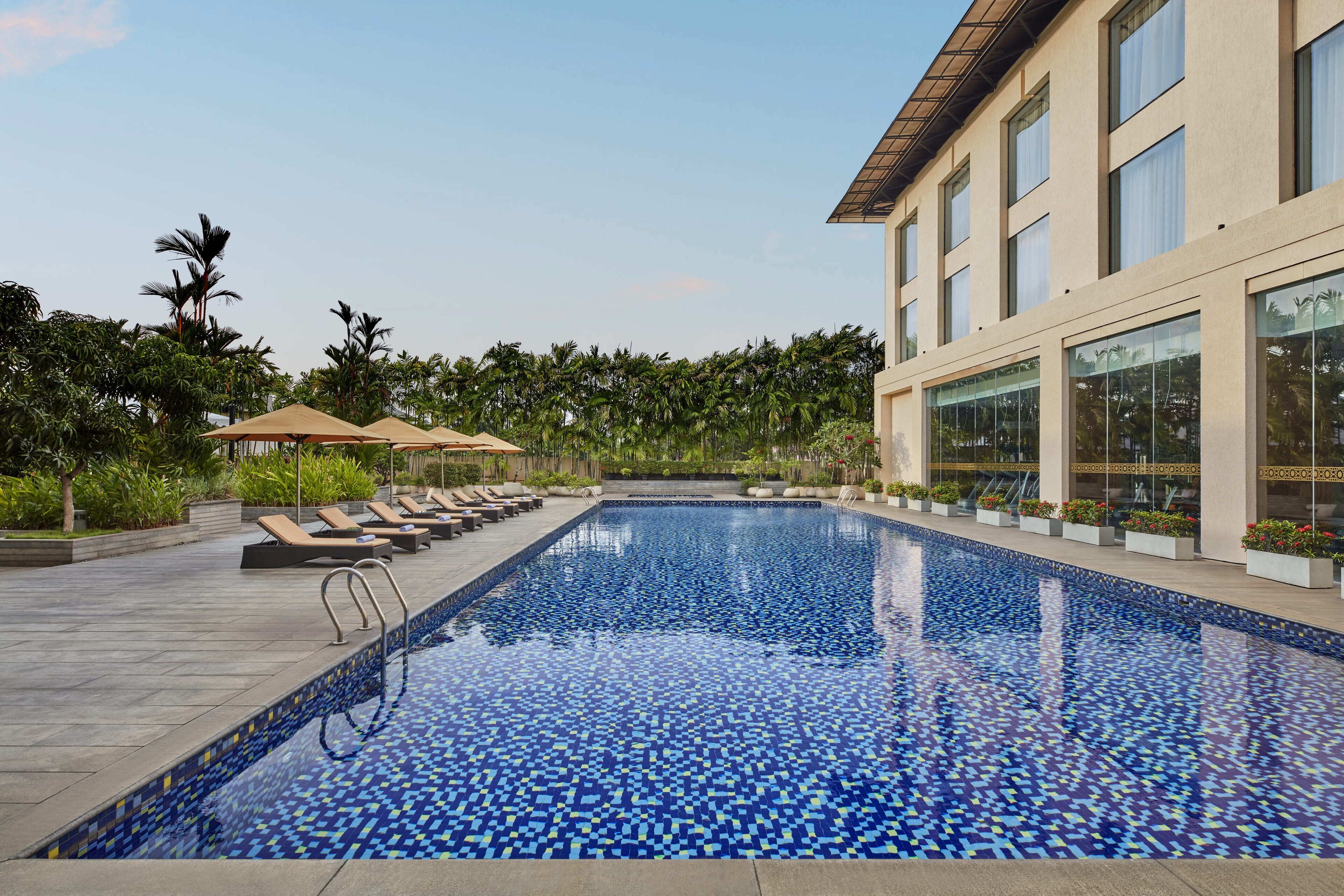 A swimming pool with tiled flooring, sun loungers, and a building with large windows.