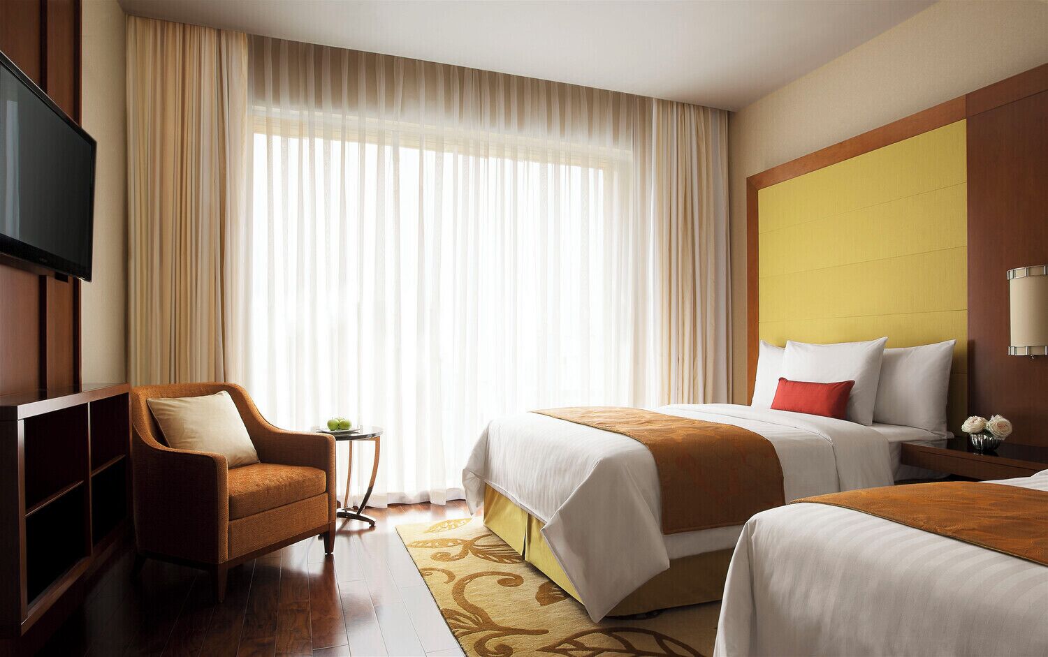Une chambre d’hôtel avec un lit, un canapé, une télévision et une fenêtre avec des rideaux.