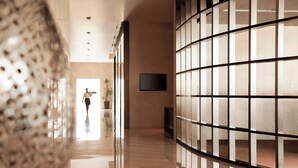 Un vestíbulo moderno de hotel con un suelo reflectante, un televisor grande montado en la pared y una persona caminando hacia la salida.