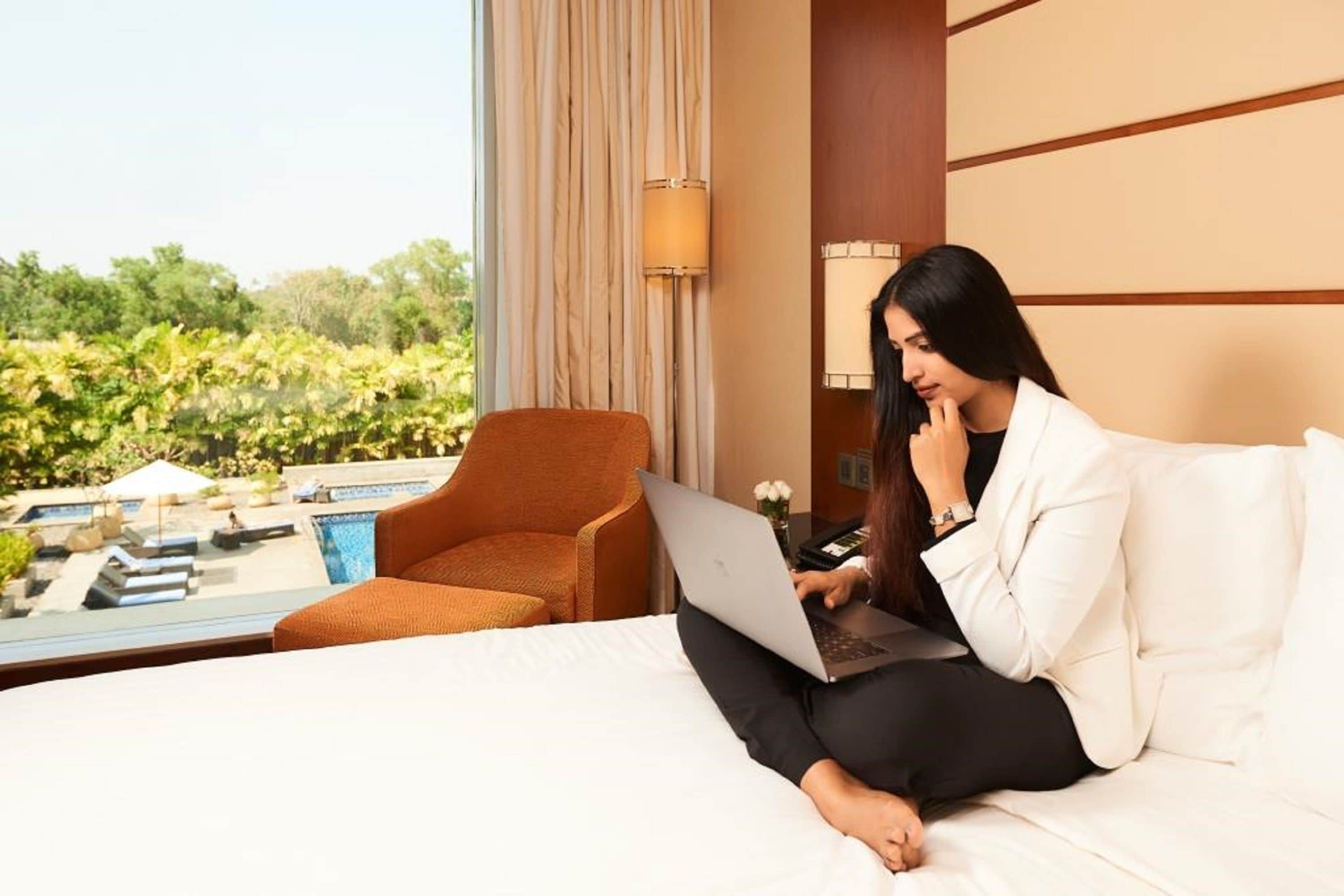 Habitación de hotel con una cama, una laptop, una silla y vistas a una piscina y follaje.
