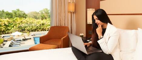 Habitación de hotel con una cama, una laptop, una silla y vistas a una piscina y follaje.