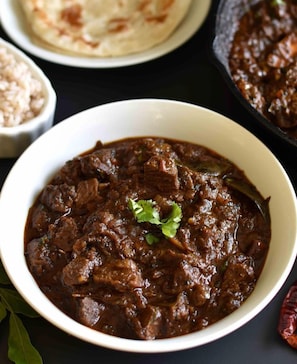 A bowl of meat-based curry with a garnish, accompanied by flatbread and a bowl of rice. - Courtyard by Marriott Kochi Airport (Aluva)