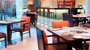 Un restaurante moderno con paredes de vidrio, mesas de madera y sillas naranjas.