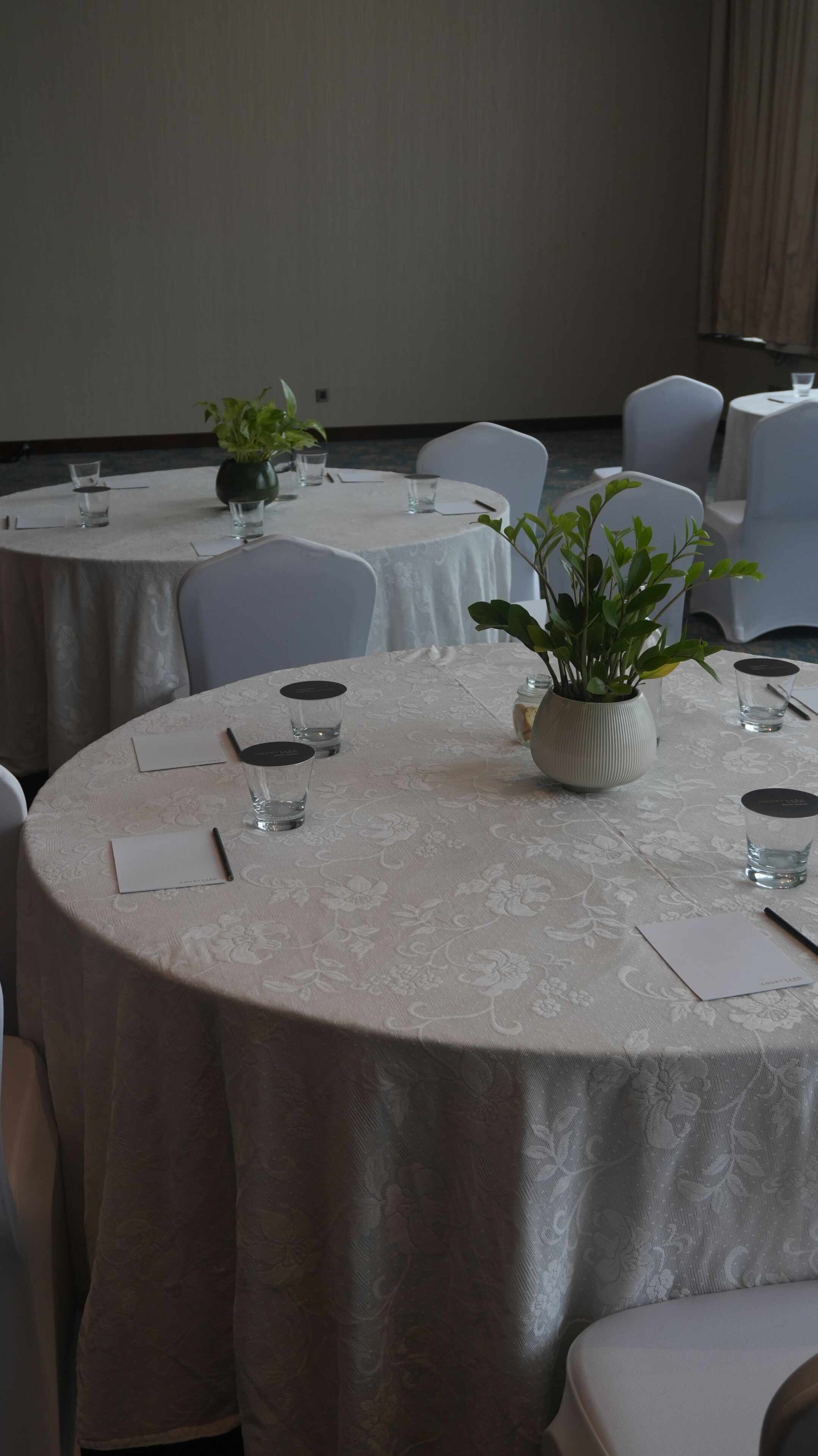 A conference room with round tables, chairs, and potted plants.