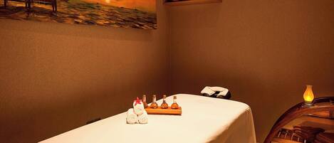 Un cuarto de spa con una camilla de masaje, toallas, velas y un cuadro de un velero en la pared.