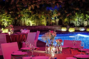 Une table à manger dressée pour un repas, avec vue sur la piscine, entourée de chaises et nappée de nappes roses.
