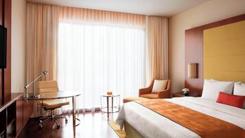 A hotel room with a large bed, a desk with a chair, a small table, and a TV.
