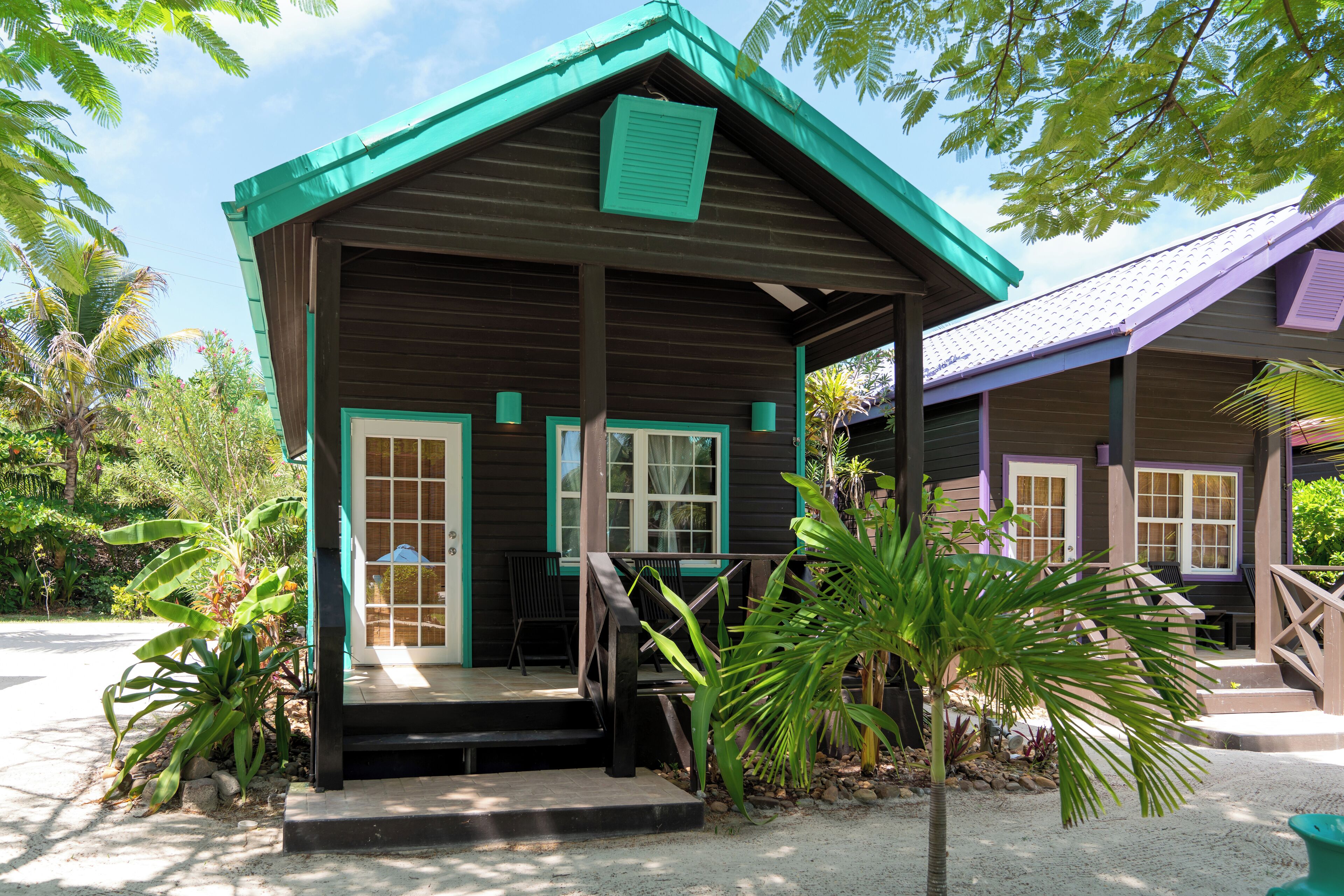 A small wooden building with a porch, surrounded by tropical plants.