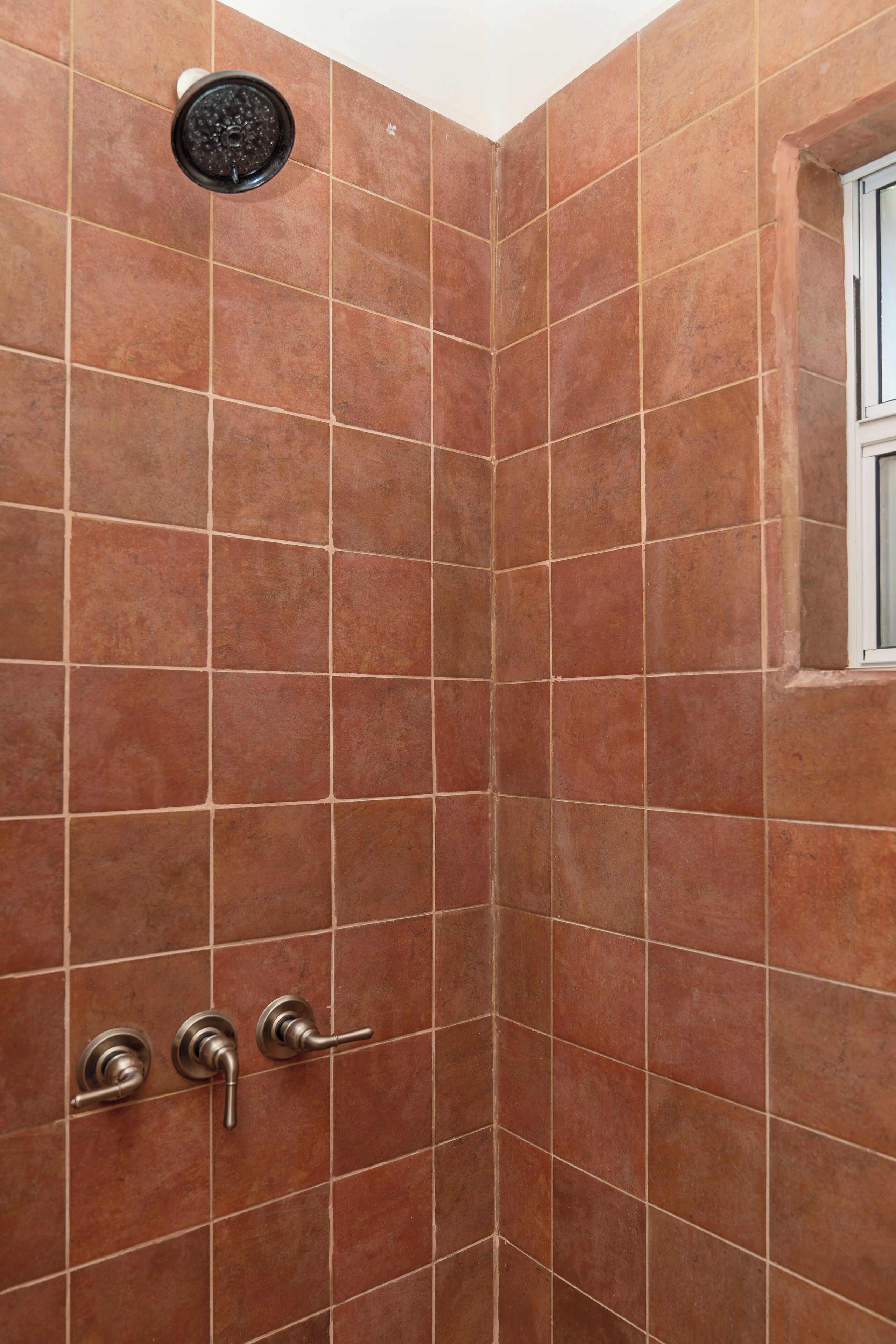 A corner shower with brown tiles and a window.