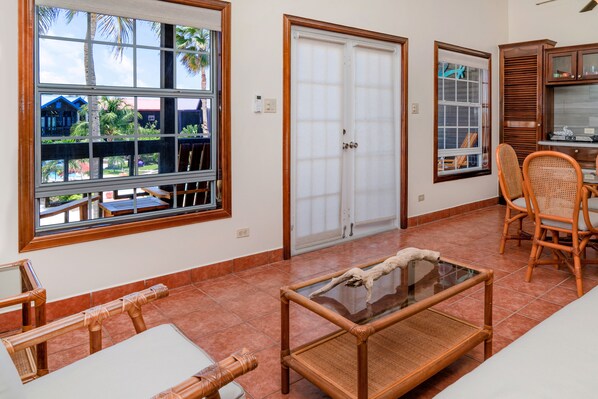 A room with a large window, a door, a glass table, and wicker furniture. - X'Tan Ha - The Waterfront Resort (San Pedro)