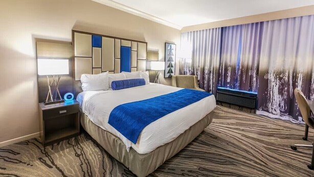Une chambre d’hôtel avec un grand lit, une table de chevet, une lampe de bureau, une chaise et une vue sur la ville par la fenêtre.