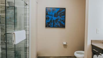 Et moderne badeværelse med en glasbrusekabine, toilet og håndvask med håndklædestang.