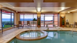 Una piscina interior con vistas al paisaje, rodeada de sillones de descanso y una pequeña terraza.