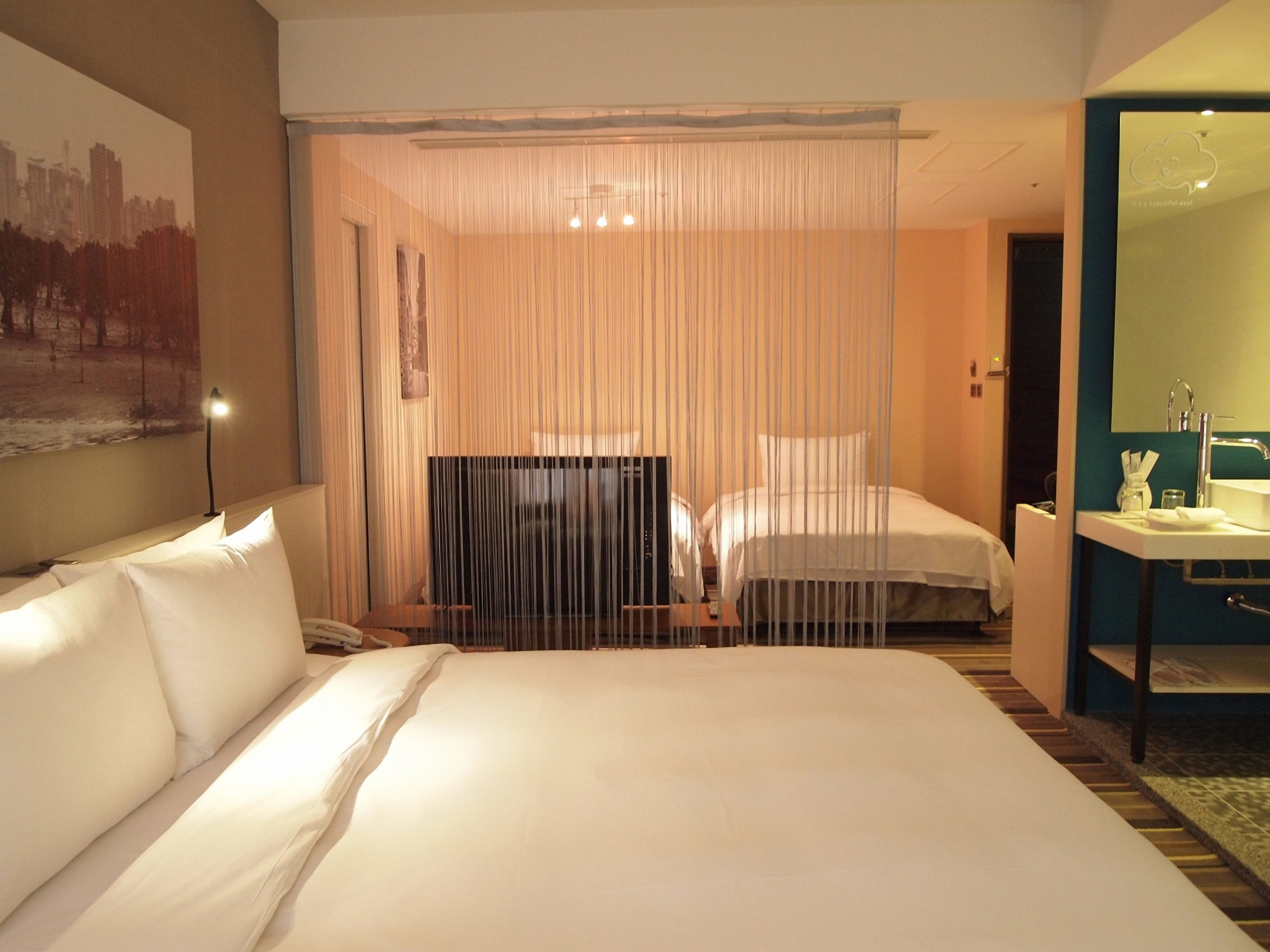 A hotel room with a large bed, a desk, a TV, and a bathroom with a mirror and sink.
