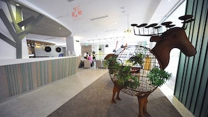 A modern interior with a reception desk, a decorative horse sculpture, and a visible staircase.