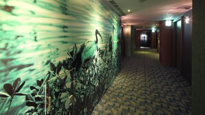 A hotel corridor with patterned carpet, a wall mural, and a long hallway leading to a door.
