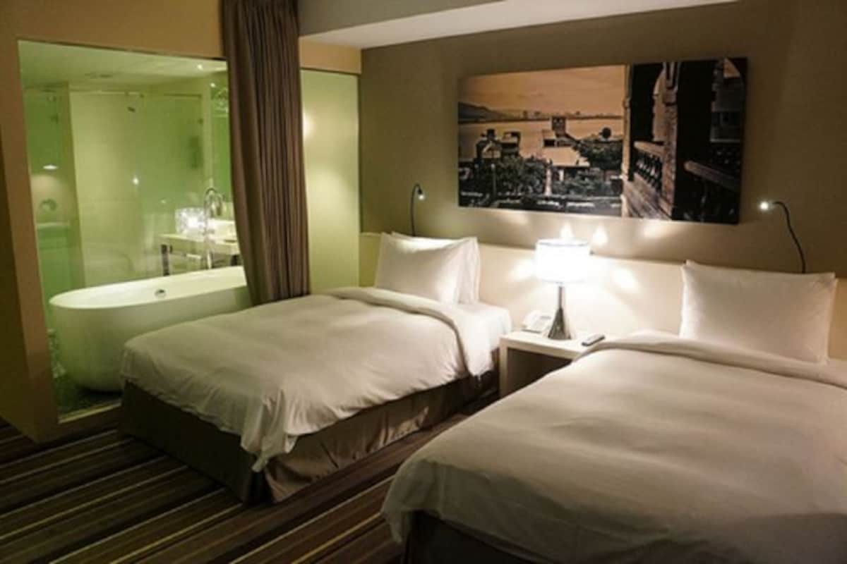A hotel room with two beds, a large mirror, a bathtub, and a painting on the wall.