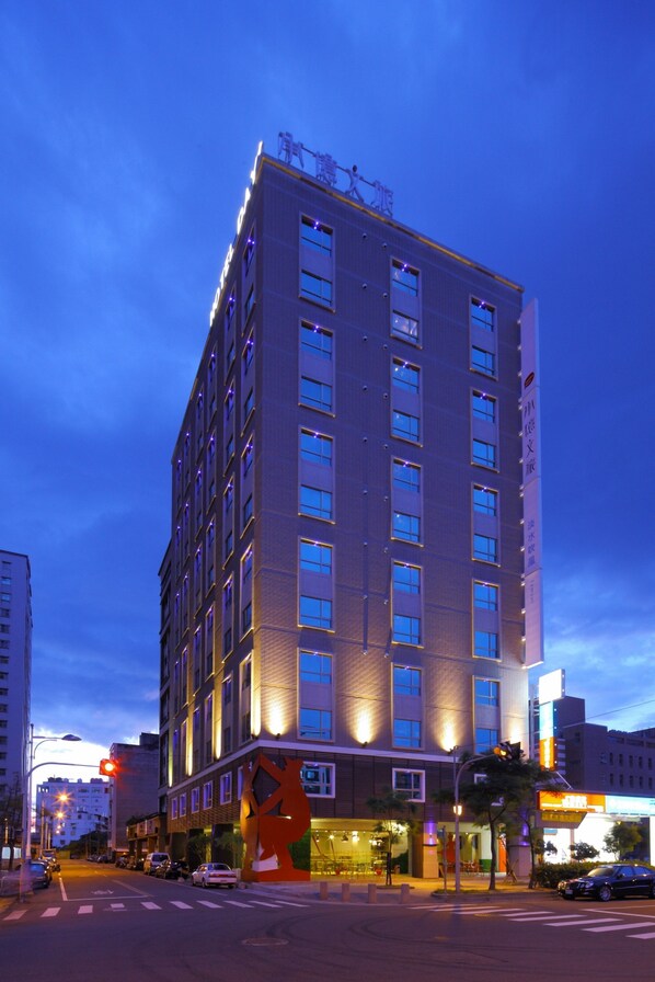 Ein mehrstöckiges Hotel mit modernem Design, das eine markante Eingangshalle und eine großzügige Außenbereich-Sitzgelegenheit bietet.