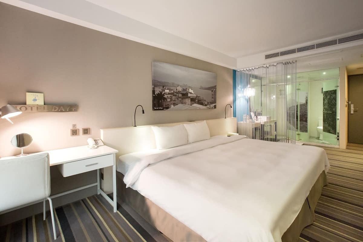 Een hotelkamer met een groot bed, een bureau met lamp, een spiegel en een schilderij aan de muur.